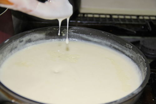 The milk is added to the flour and butter mixture a little at a time, allowing each batch to be absorbed before adding more milk. Constant stirring is required. The mixture will thicken suddenly, and so keep stirring vigorously.