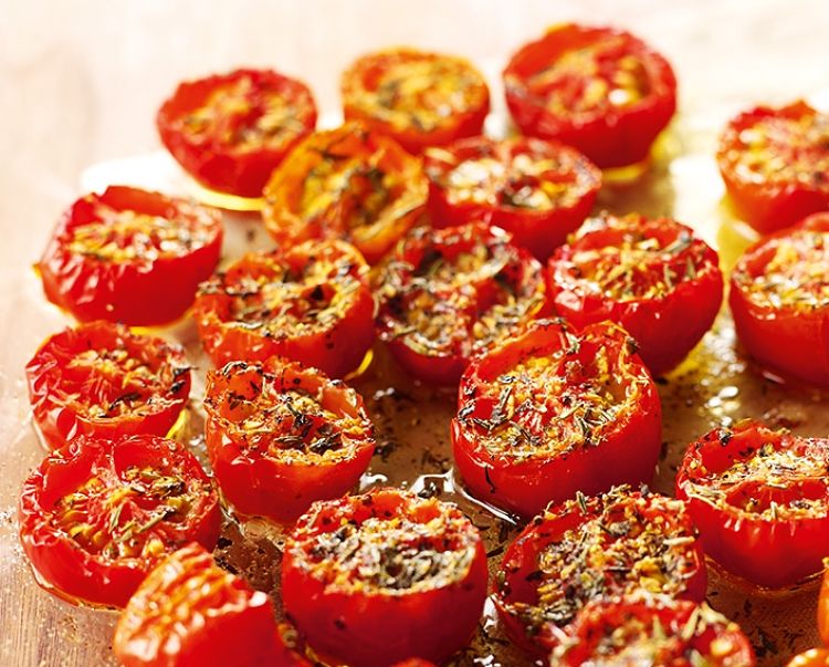 Tomatoes sprinkled with herbs and spices ready for drying in the oven